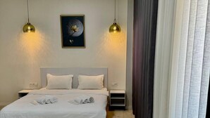 A modern bedroom with a large bed, two bedside tables, a round table, and a painting on the wall. - Bogdon Grand Hotel (Tashkent)