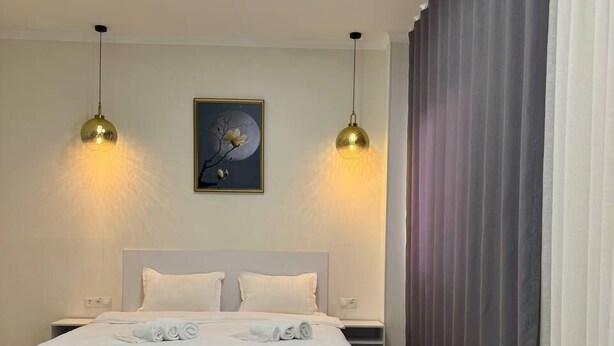 A modern hotel room with a large bed, two pendant lights, a round table, and a painting on the wall. - Bogdon Grand Hotel (Tashkent)