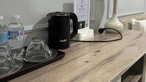A hotel reception area with a wooden counter, a black Sonifer coffee maker, water bottles, a white lamp, and a framed picture on the wall. - Bogdon Grand Hotel (Tashkent)