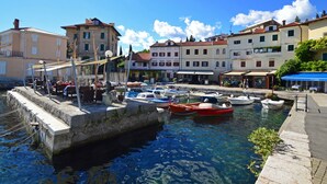 A marina with boats docked, a stone wall, and buildings with balconies and shops.