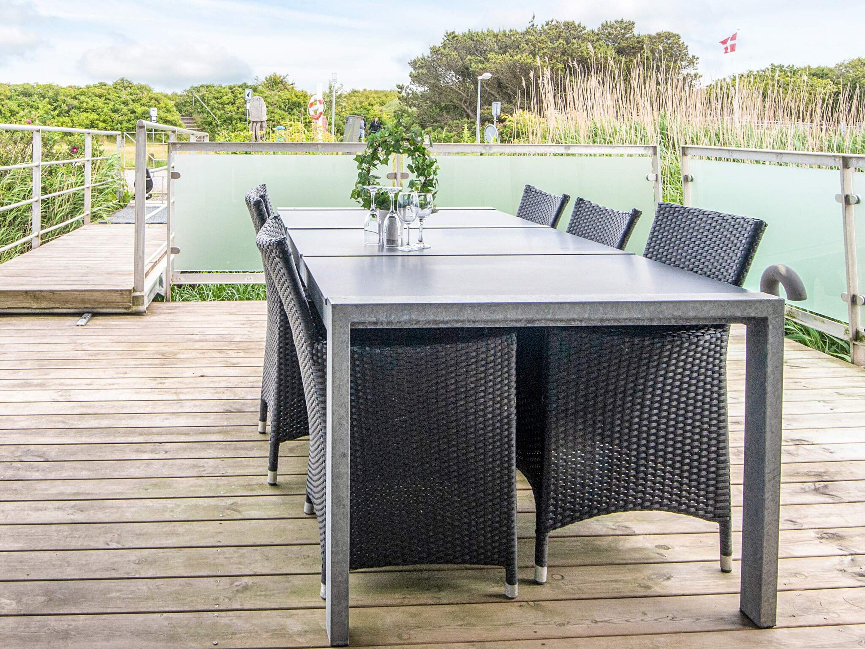 Une table rectangulaire pour l’extérieur, accompagnée de six chaises, entourée d’une terrasse en bois.