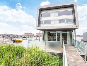 A modern building with a glass facade and a wooden deck leading to a dock area with boats. - 5 Star Holiday Home in Hemmet (Hemmet)