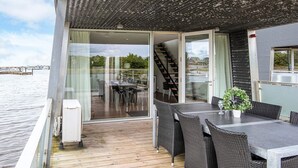 A deck with a table and chairs, a potted plant, and a view of the water and buildings in the background. - 5 Star Holiday Home in Hemmet (Hemmet)