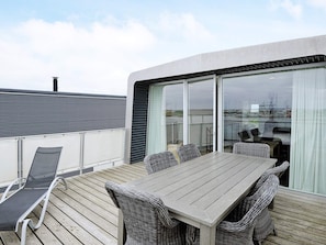 A deck with a table and chairs, a sun lounger, and a glass door leading to a view of the sea.