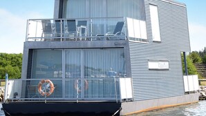 A modern houseboat with a flat roof, large windows, and a lifebuoy at the bow. - 5 Star Holiday Home in Hemmet (Hemmet)