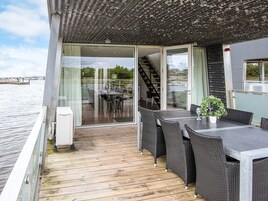 Um terraço com mesa e cadeiras, um vaso de planta e vista para a água e edifícios ao fundo.