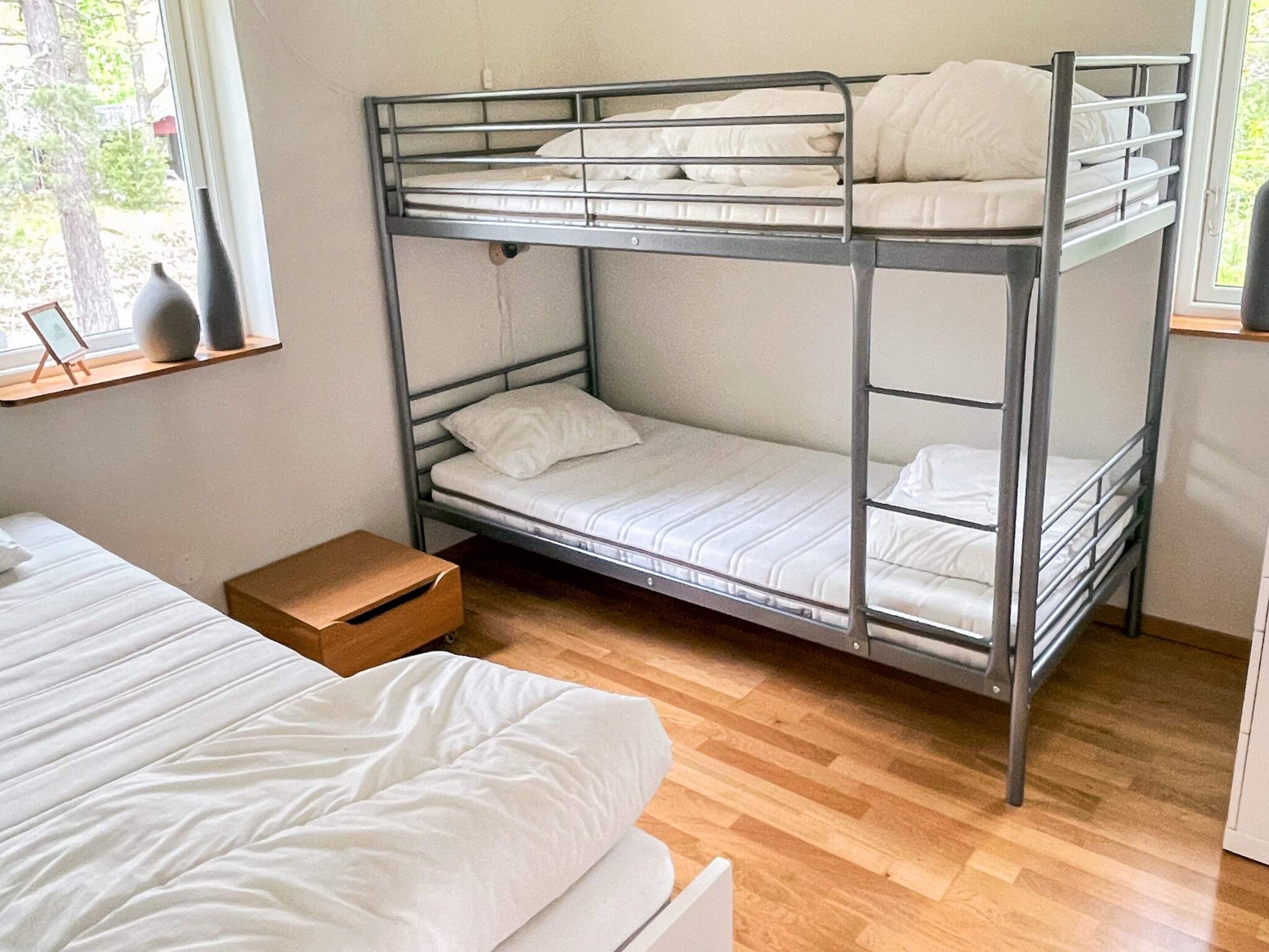 A bunk bed with two levels, a wooden floor, and a window with a view of trees.