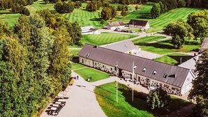 An aerial view of a golf course with a clubhouse, surrounded by trees and a body of water in the background. - 5 Star Holiday Home in Osby (Osby)