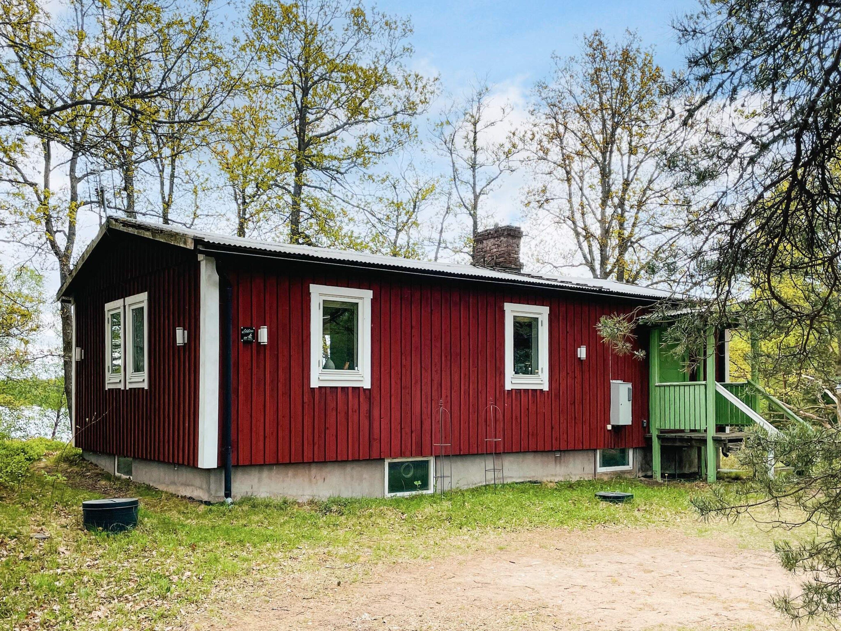 A red wooden cabin with a green staircase, surrounded by trees.
