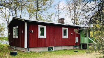 A red wooden cabin with a green staircase, surrounded by trees.