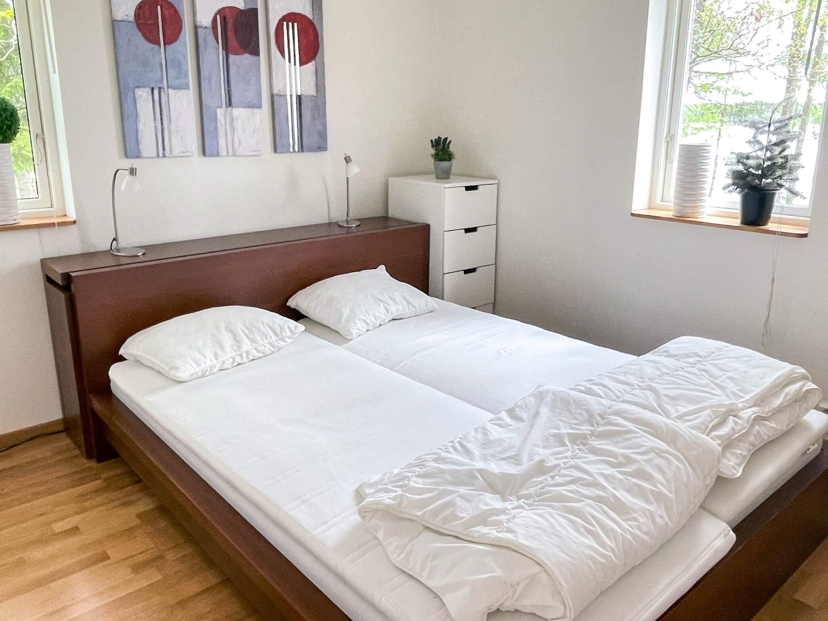 A double bed with white bedding, a nightstand with a lamp, and abstract wall art.
