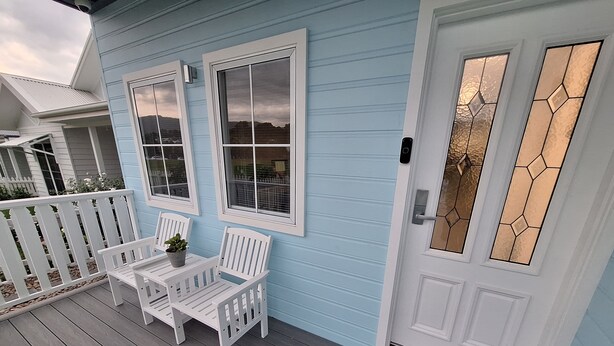 A porch with two white benches and a small table, a white door with a glass panel, and a white picket fence.
