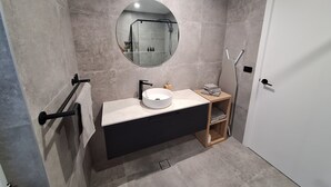A modern bathroom with a round mirror, a white sink, black cabinet, and a towel rack.
