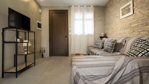 A bedroom with a bed, a TV, a shelf, and a brick wall. - Rianou Apartment (Chania)