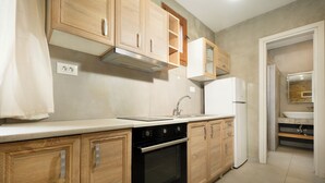 A modern kitchen with wooden cabinets, a stainless steel range hood, a built-in oven, and a white refrigerator. - Rianou Apartment (Chania)