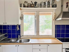 A kitchen with a double sink, cabinets, and a window with a view of greenery.