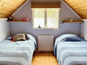 A bedroom with two beds, a window, a radiator, and wooden beams on the ceiling.