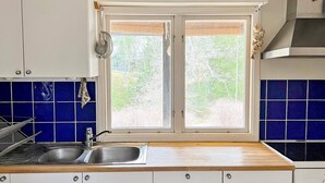 A kitchen with a double sink, white cabinets, blue tiles, and a window with a view of greenery. - 5 Person Holiday Home in Ingaro (Ingaro)