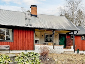 A red wooden house with a metal roof, a green door, and a visible number '7' on the front. - 5 Person Holiday Home in Ingaro (Ingaro)