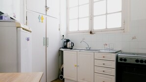 Ett litet kök med vita skåp, en diskho, en spis och ett fönster.