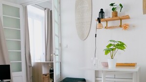 Ett rum med trägolv, ett vitt skrivbord med två stolar, en grön bänk, en surfbräda på väggen och en växt på en hylla.