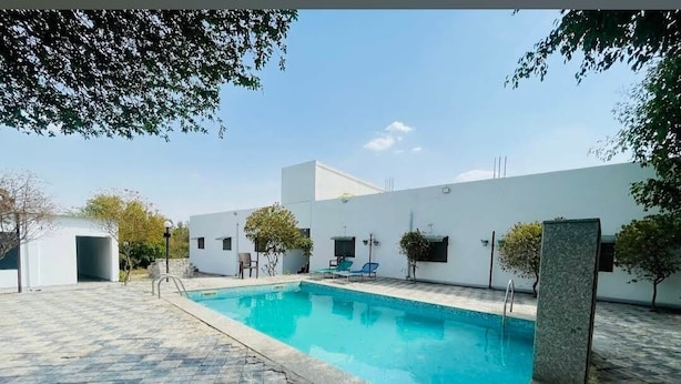 Una piscina con bordeado de baldosas, rodeada por un edificio blanco con ventanas y una puerta.