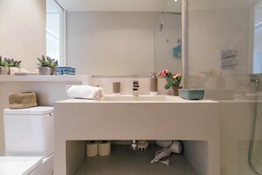 Ein modernes Badezimmer mit einem weißen Waschbecken, einer Duschkabine aus Glas und einer Toilette.