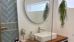 Een moderne badkamer met een backsplash van visgraat tegels, een ronde spiegel, een wit wastafelmeubel, een handdouche, een wasmachine en een hangplant.