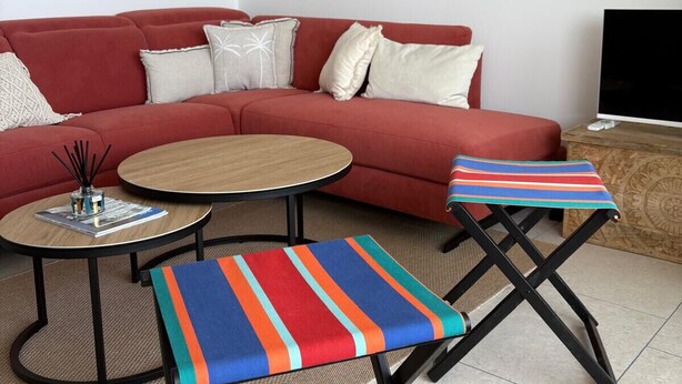 Een moderne woonkamer met een rode bank, twee ronde salontafels en een kleurrijk gestreept voetenbankje.