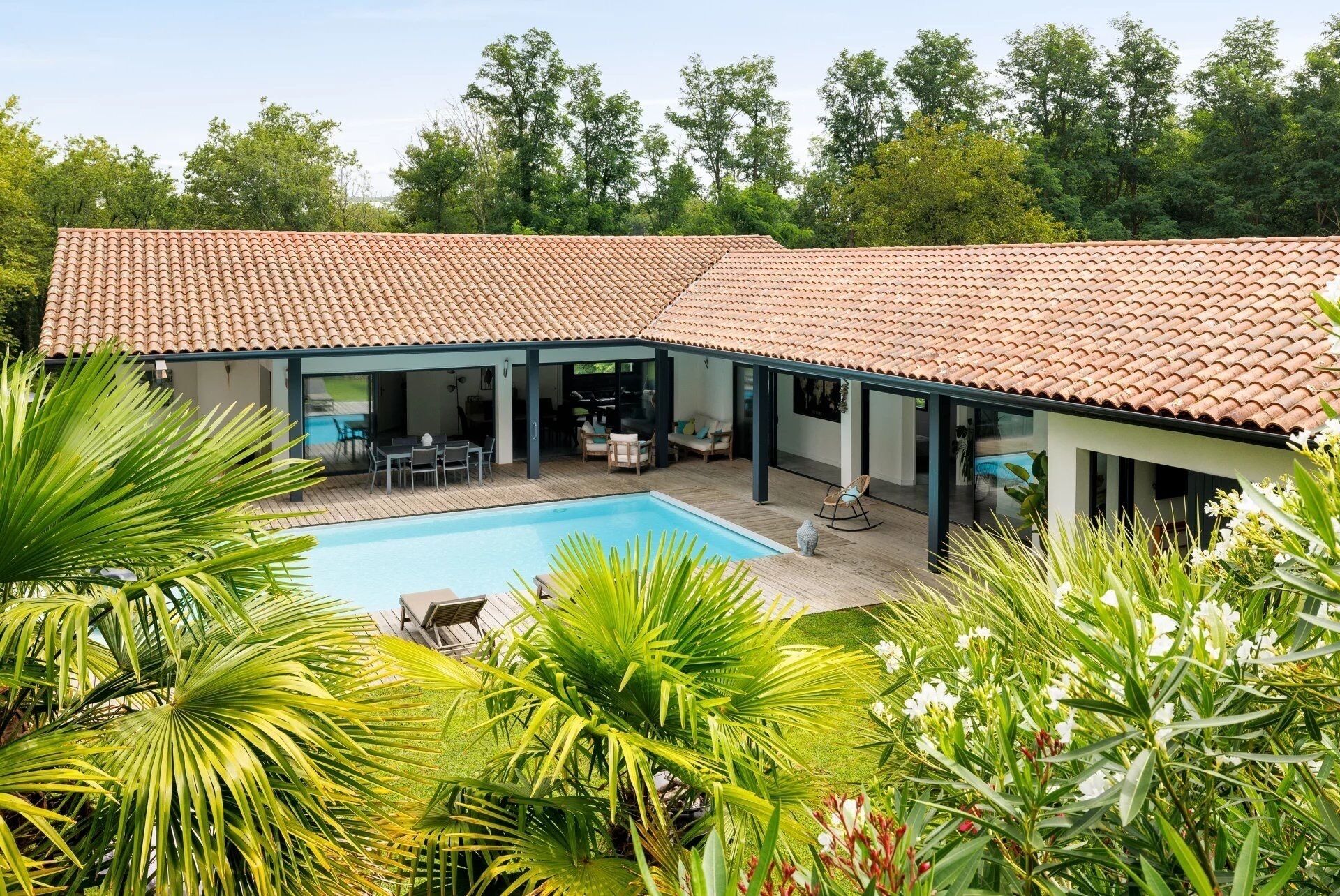 A modern house with a swimming pool, covered patio, and lush greenery.