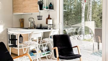 A modern kitchen with white cabinetry, a dining area with two black chairs, and a view of a forest through a glass door.