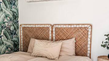 A bed with a woven headboard, a shelf above it, and a wall with a tropical leaf pattern.
