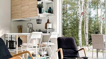 A modern kitchen with white cabinets, a coffee machine, and a dining area with white chairs and a glass table.