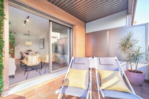Un patio soleado con dos sillones de descanso, una planta en maceta y un ventanal de vidrio que da a un comedor interior.