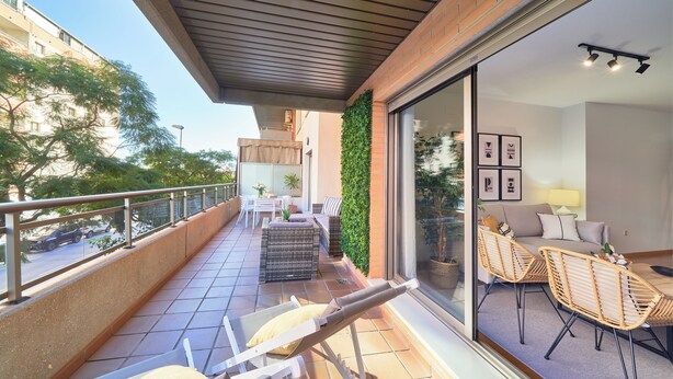 A balcony with a seating area, a dining table, and a view of the street. - Solaga - Parque Litoral (Málaga)