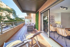 A balcony with a seating area, a dining table, and a view of the street. - Solaga - Parque Litoral (Málaga)