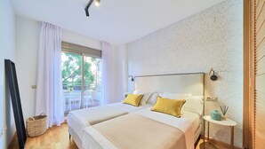 A hotel room with two beds, a small table with a lamp, a wicker basket, and a view of the outdoors. - Solaga - Parque Litoral (Málaga)