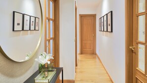 A hallway with wooden flooring, framed pictures on the walls, a mirror, and a vase with flowers. - Solaga - Parque Litoral (Málaga)
