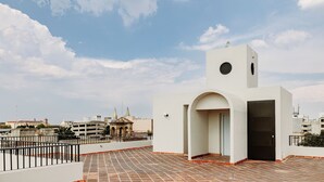 Une terrasse sur le toit, avec un bâtiment blanc, une porte noire et une vue sur des bâtiments éloignés.