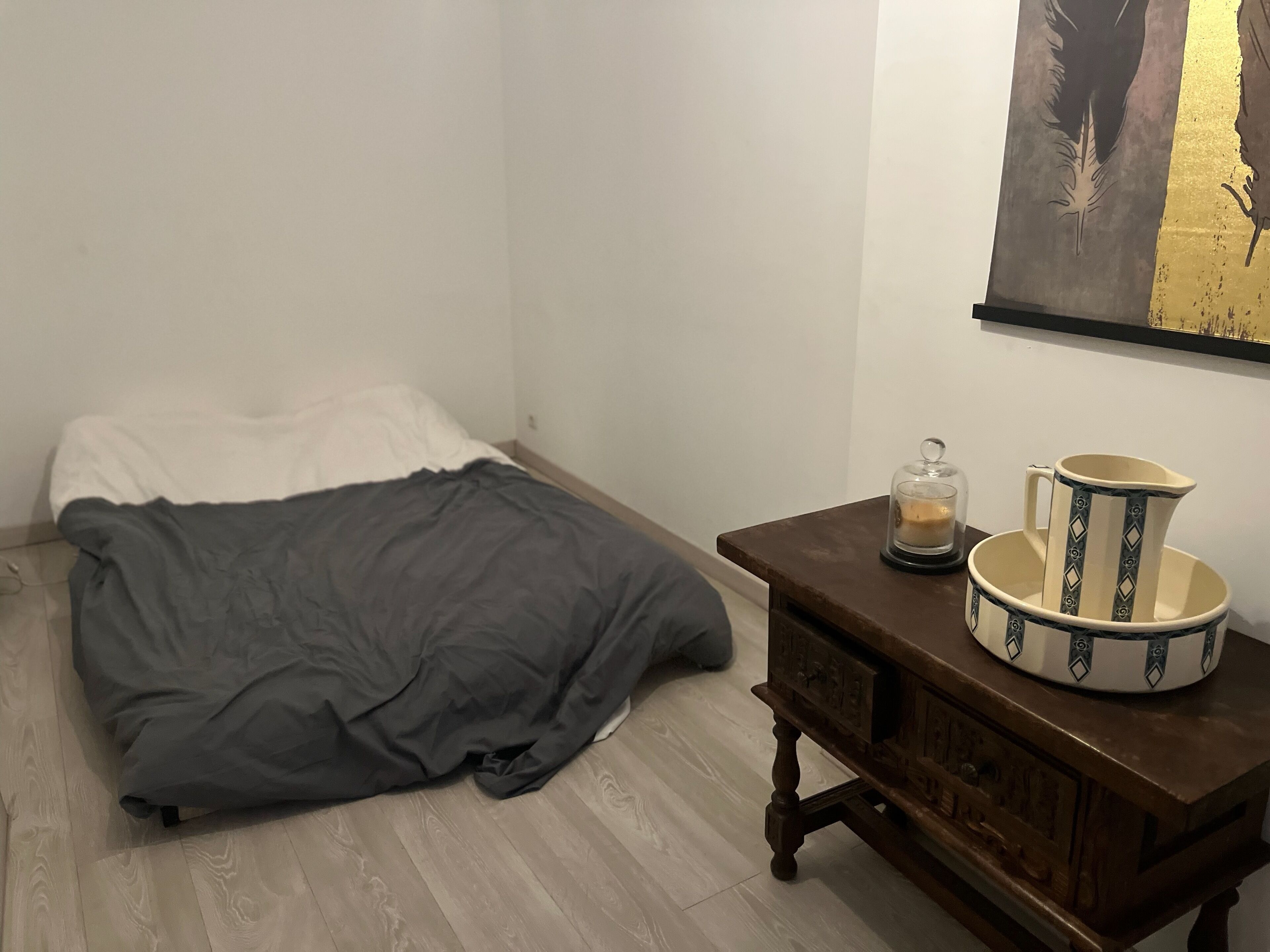 A bedroom with a bed, a wooden nightstand with decorative items, and a painting on the wall.