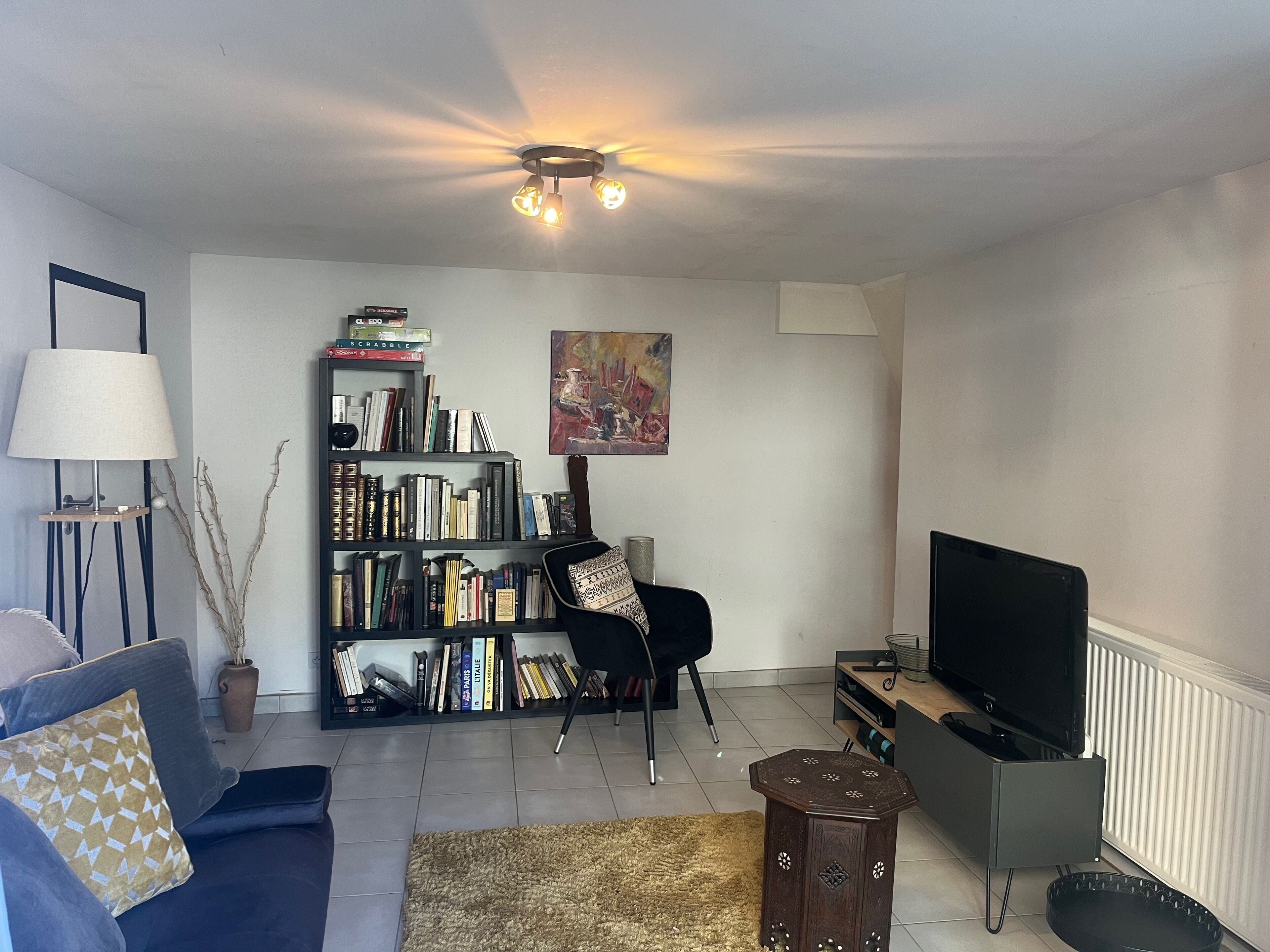 A living room with a sofa, a bookshelf, a painting, a lamp, and a television.