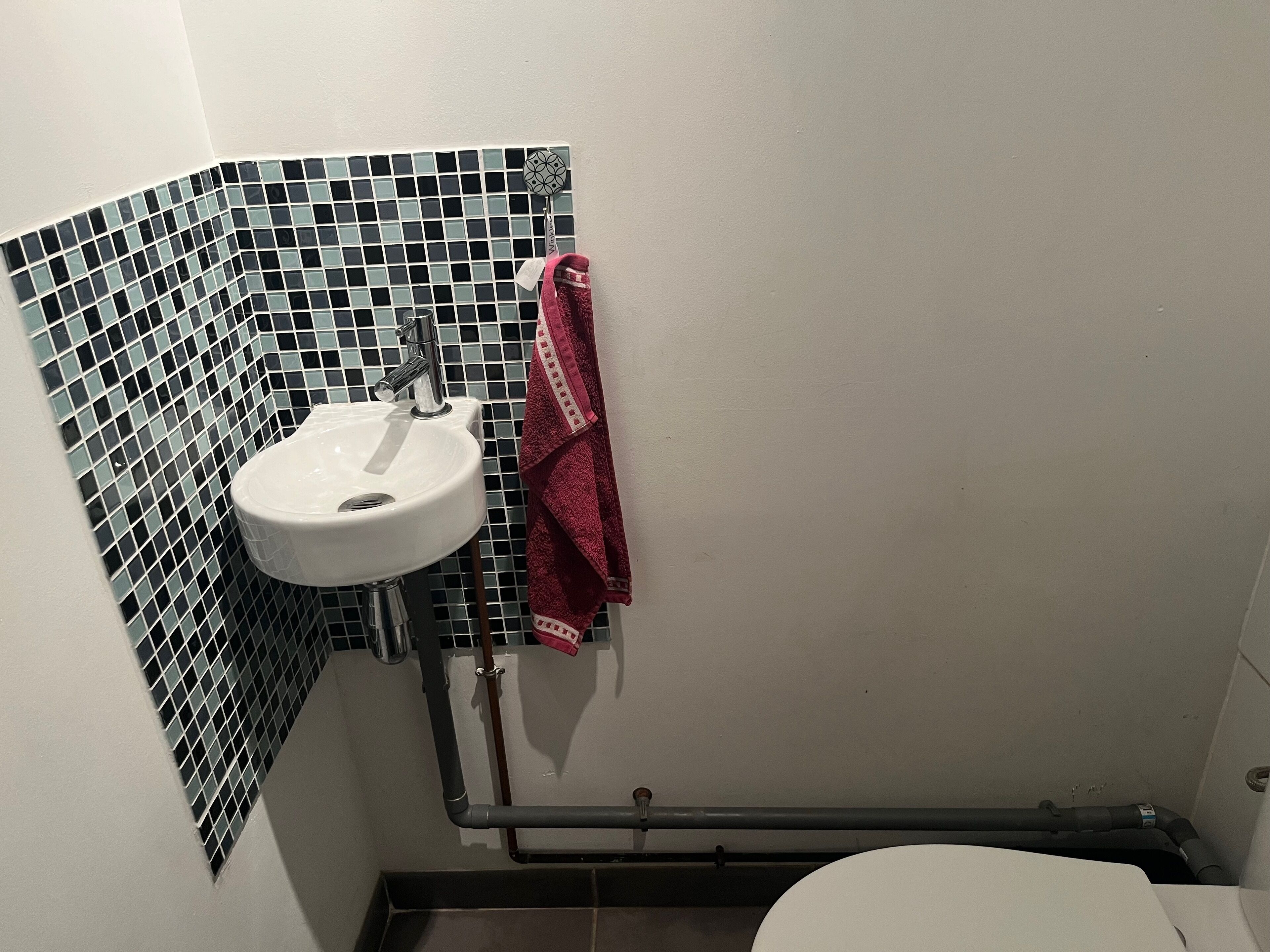 Une salle de bain avec un lavabo blanc, des carreaux de mosaïque noirs et blancs, et une serviette rouge accrochée au mur.