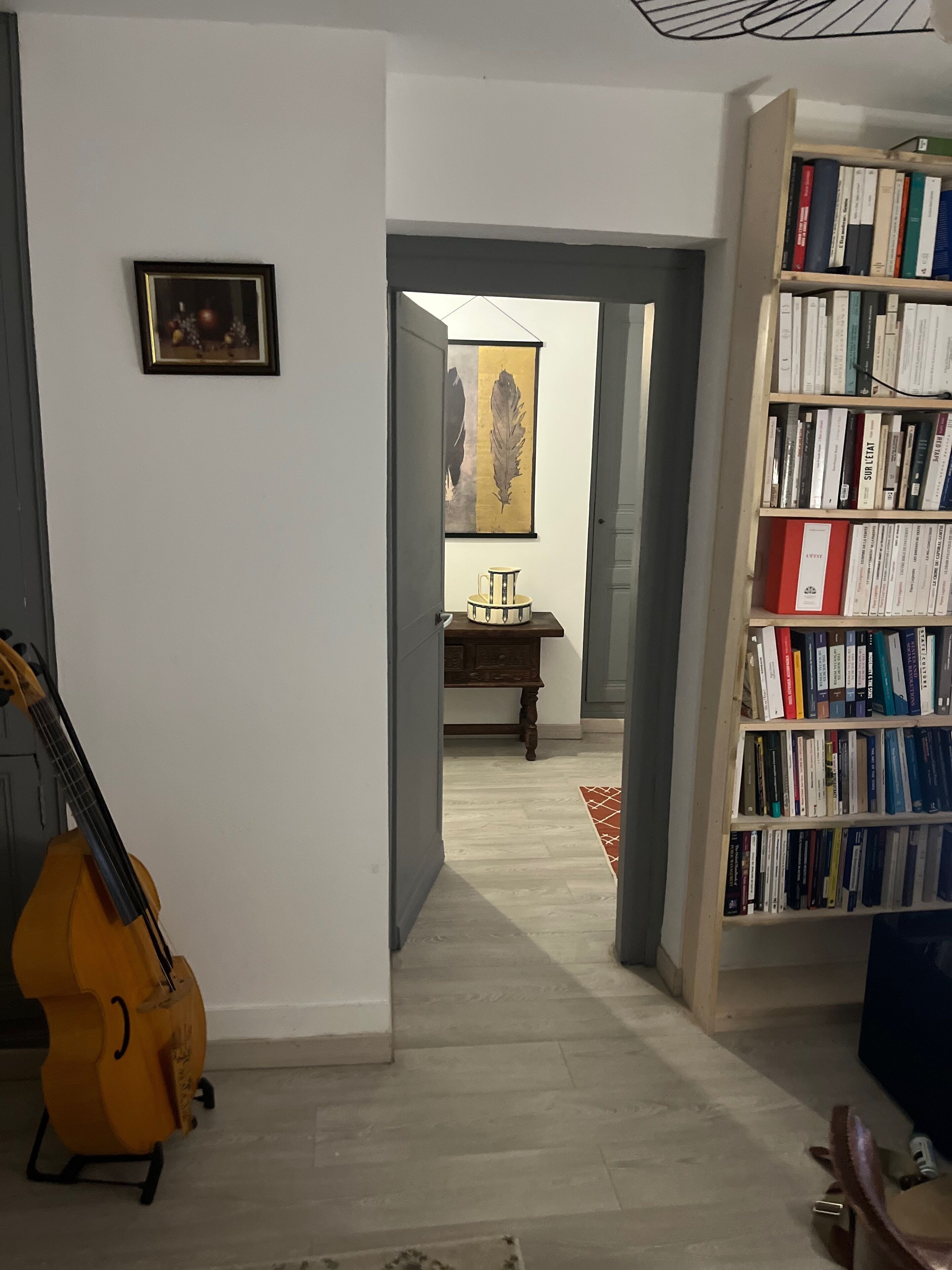 A room with a bookshelf, a guitar, a framed picture, and a desk with a chair.