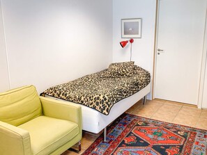 A small room with a single bed, a yellow chair, a patterned rug, and a framed picture on the wall.
