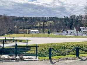 Un paisaje rural con una carretera pavimentada, una zona cercada y casas al fondo.