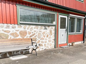Un muro de piedra con un banco, un edificio rojo con una puerta y una ventana.