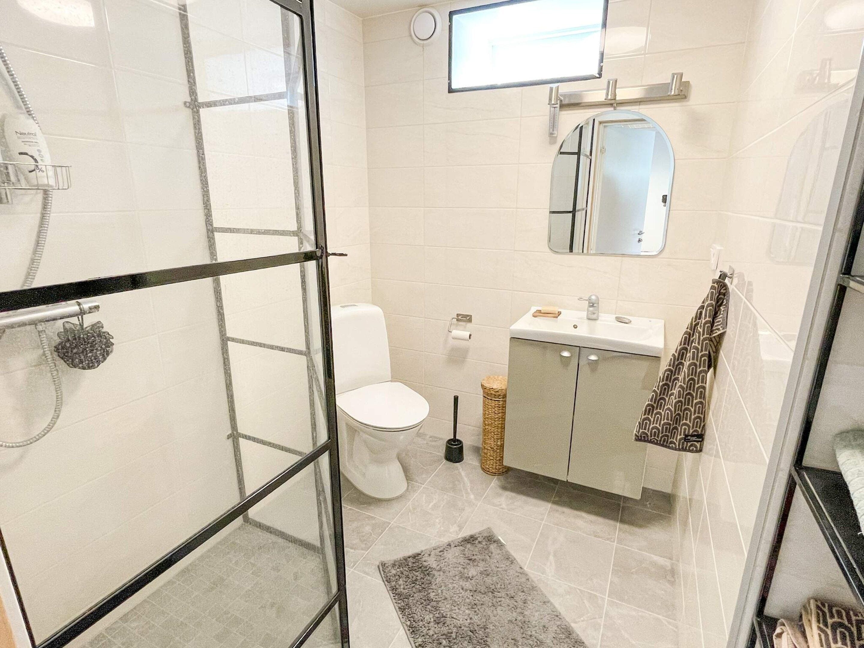 Un baño con cabina de ducha de vidrio, inodoro, lavamanos con espejo y una toalla colgada en la pared.