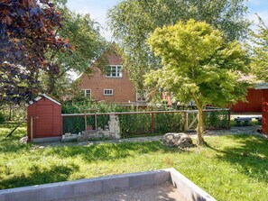 Un patio trasero residencial con un cobertizo rojo, un árbol y un muro de ladrillo.