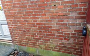 Una pared de ladrillo con una puerta metálica y un escalón que conduce a un nivel inferior.