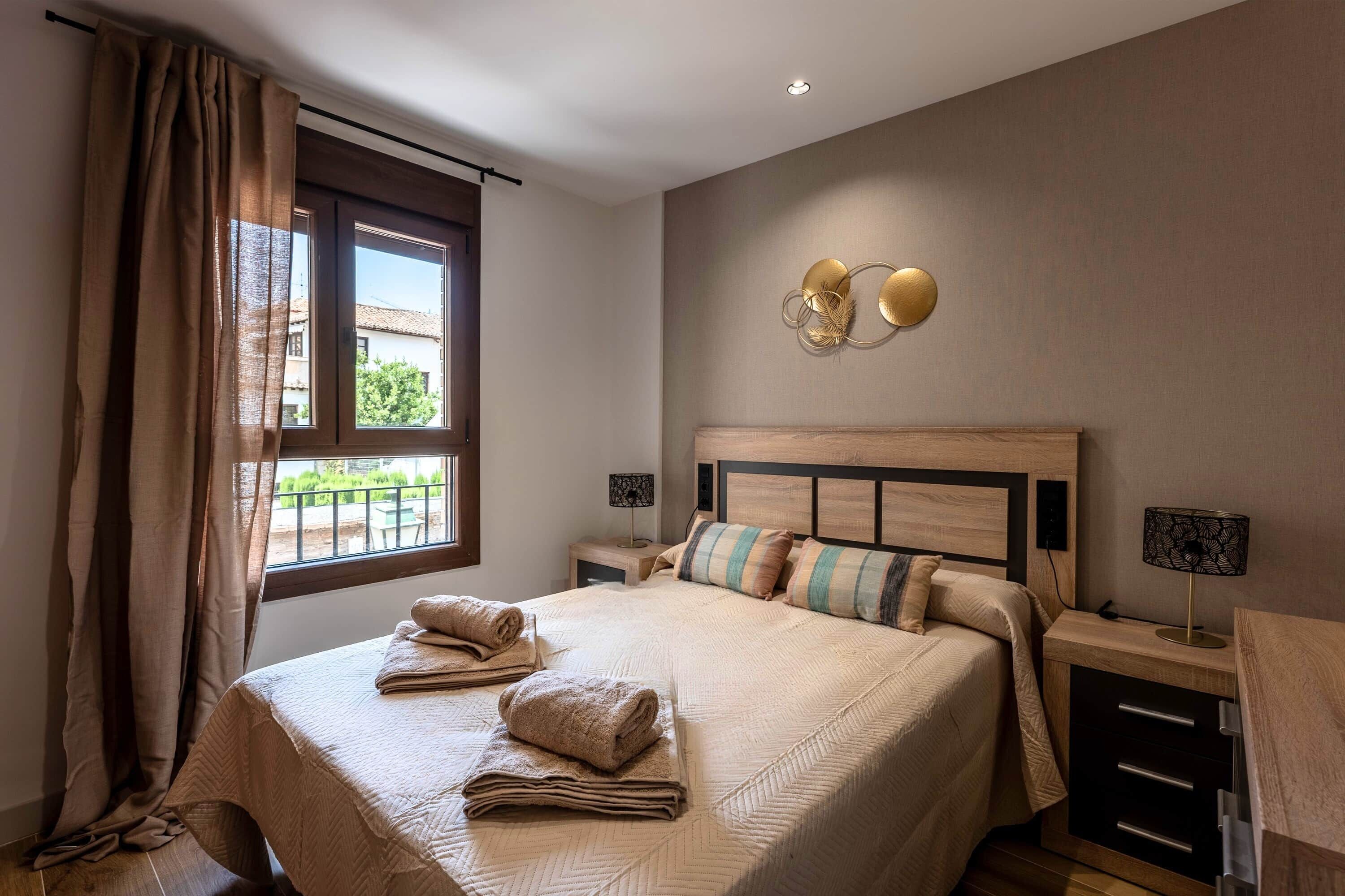 Quarto com cama grande, duas mesas de cabeceira, luminária na parede e janela com cortinas.